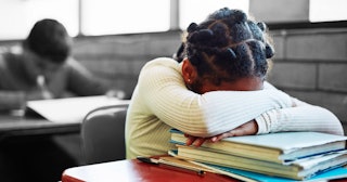 A young girl at a school desk feeling overwhelmed, facing her hands and head on books.