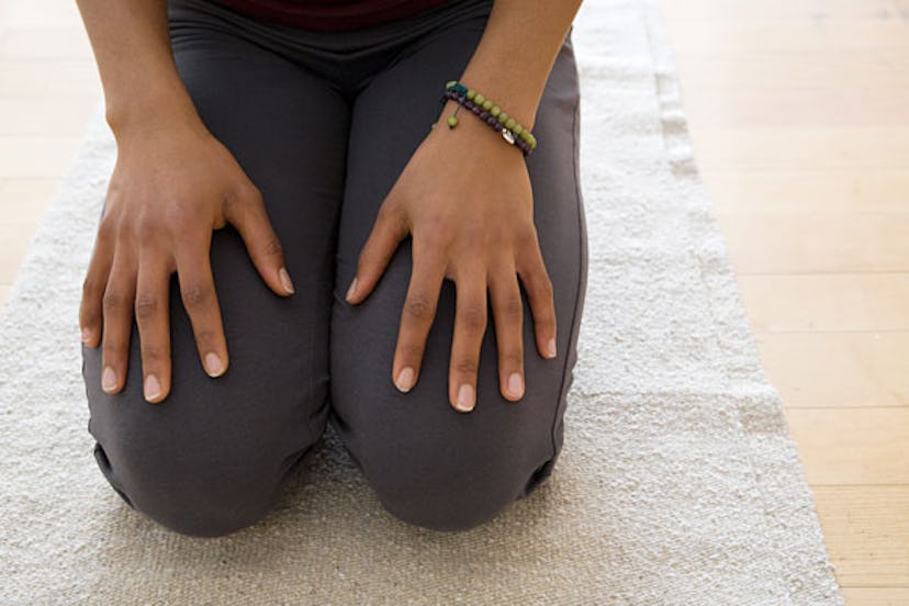 A woman is sitting on the floor with hands on her knees, her thighs being the focal point 