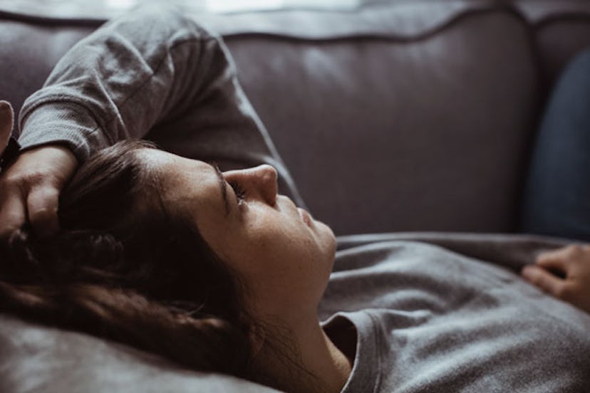 A woman lying on a couch and holding her head while staring at the ceiling