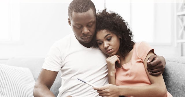A man and a woman sitting hugged on a couch with a sad facial expression while the woman is holding ...