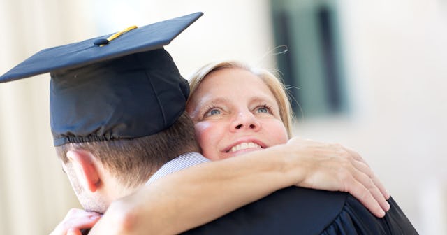 A mom hugging her teen son, who's wearing a school graduation gown and hat.