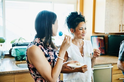 Two middle-aged sisters who have an abusive mother smiling while eating in the kitchen 