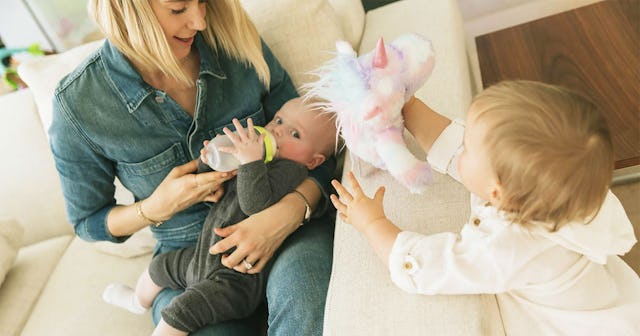 Mom breastfeeding her baby while her toddler is playing around 