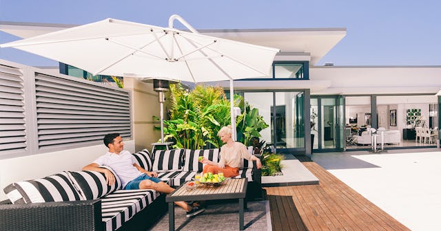 A man and a woman sitting on a navy and white striped sofa underneath a large white patio umbrella