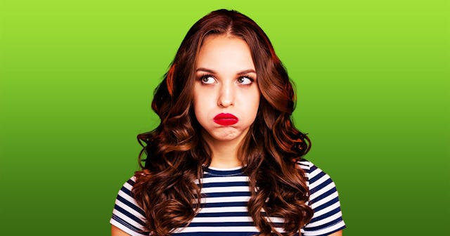 A woman with long brown hair in a striped shirt puffing her cheeks and looking annoyed