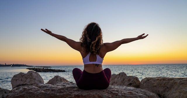 Kegel exercises, woman sitting in front of water during sunset with arms outstretched