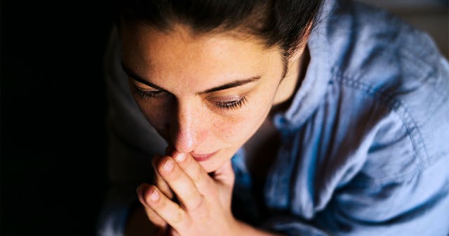 Woman sitting alone in the dark with hands on her mouth