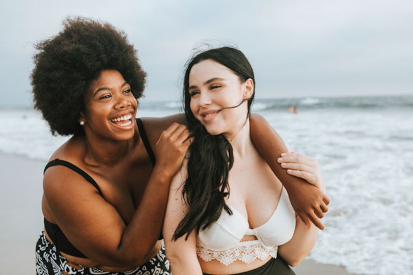 Two women smiling on a beach in bikinis. 