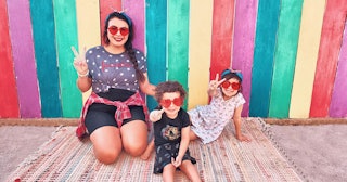 A Social media influencer mom and two girls posing in front of a rainbow wall while wearing heart-sh...