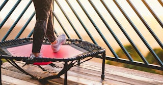 A woman standing on a red and black fitness trampoline on a balcony