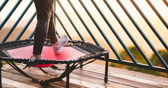 A woman standing on a red and black fitness trampoline on a balcony