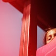 A scared brown-haired kid looking from the top of a red slide in the playground