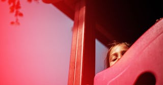 A scared brown-haired kid looking from the top of a red slide in the playground