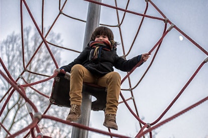A young brown-haired boy looking down from the rope climber on the playground 