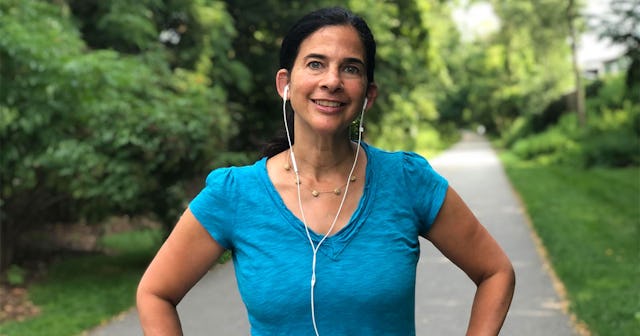 A woman in a blue shirt with white earphones standing and smiling after completing exercise in a par...