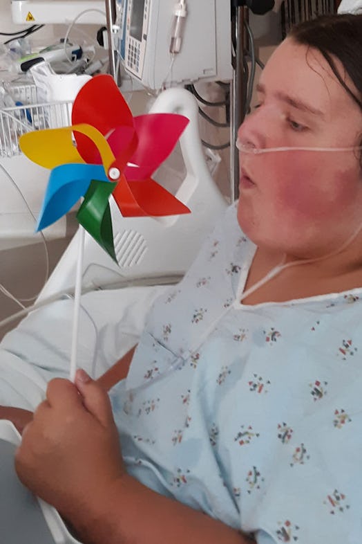 Melanie Hall's daughter in a hospital bed in a blue hospital gown blowing into a wind spinner toy