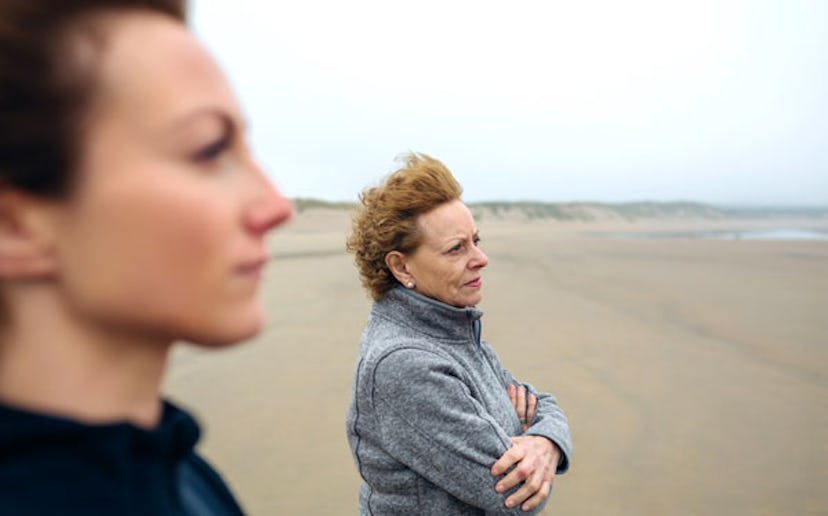 A daughter standing next to her mom while looking at the sea on the beach in autumn