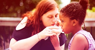 A mother is giving her neurodiverse child a glass of water to drink at a park.