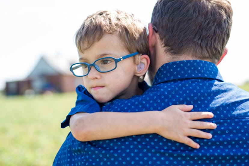A father in a blue shirt is carrying his neurodiverse child, who's wearing a blue t-shirt, glasses, ...