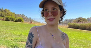 Halsey wearing a pink tank top, brown sunglasses, and beige cap outside during a sunny day