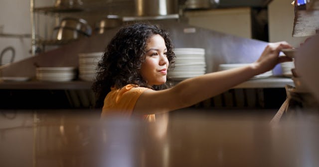 A curly-haired teenage girl in a restaurant reaching for a plate