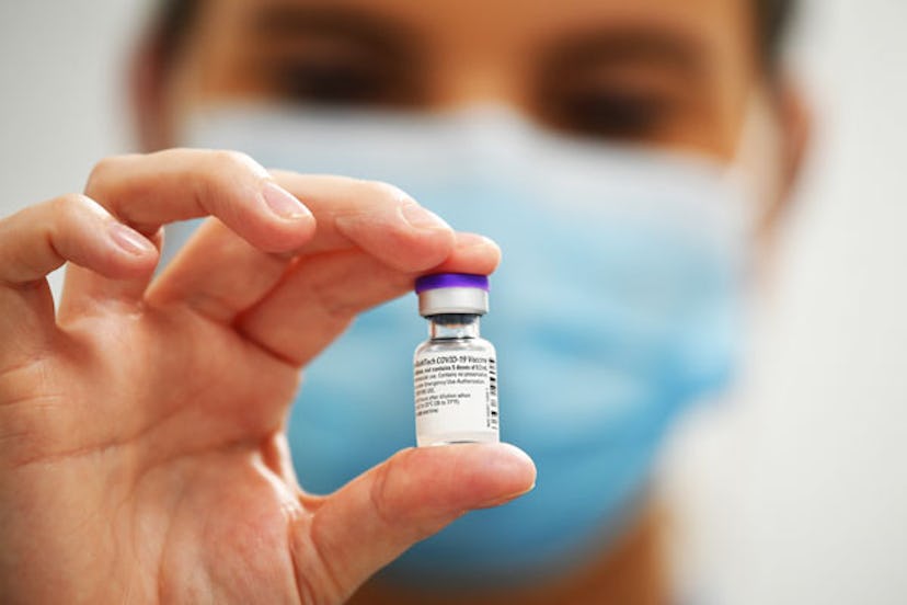 A woman holding a vial with the COVID-19 vaccine in it with her face blurred in the background