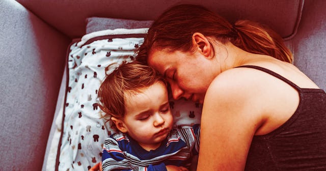 A brunette woman who is not okay in a black tank top in bed next to her child