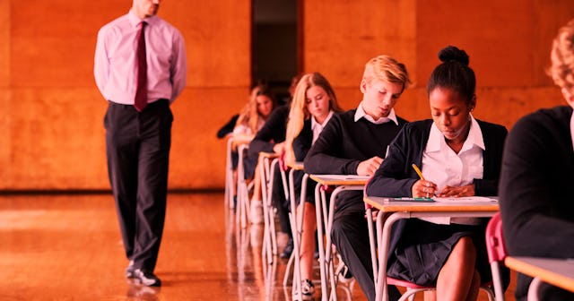 Kids sitting in line at the private school desks while teacher is walking beside them