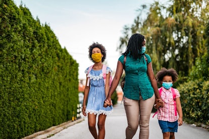 A woman walking her two children to school while they're all wearing face masks instead of virtual s...