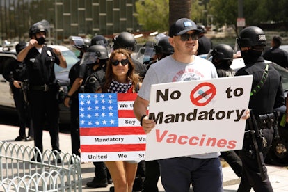 Two people protesting with signs that say vaccine mandates are violating rights and they don't want ...