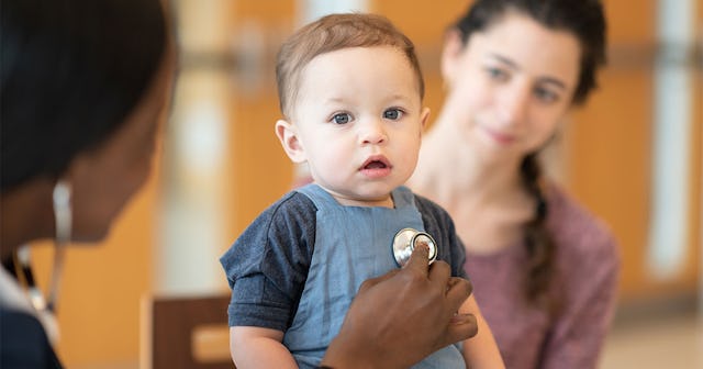 A brown-haired kid wearing a blue tracksuit while being at the doctor with his mother