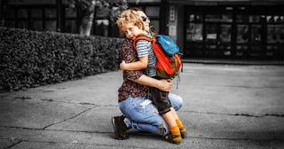 A mom kneeling and hugging her son in front of a building