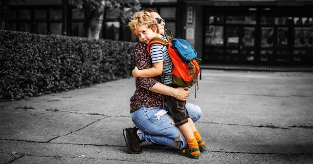 A mom kneeling and hugging her son in front of a building
