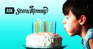 A  boy in a blue shirt, blowing colorful candles on his white-frosted birthday cake, with a blue bac...