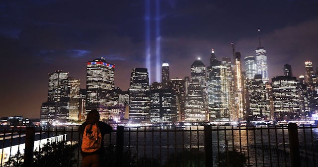 A woman in a black hoodie and an orange backpack leaning on a railing and watching New York City at ...