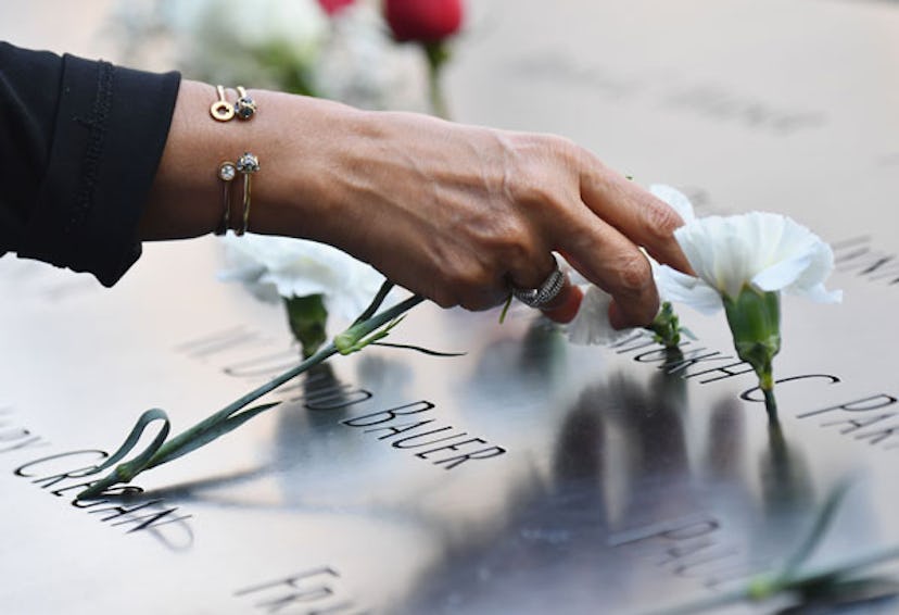 A woman's hand is placing white flowers on the victims' names at the 9/11 Memorial