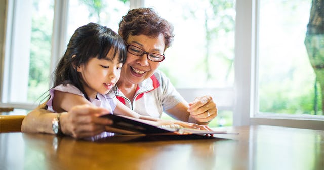 A smiling woman cheerfully reads a book with her granddaughter.