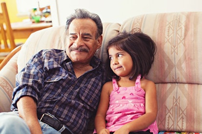 A smiling man sitting on a couch in a hug with his little granddaughter. 