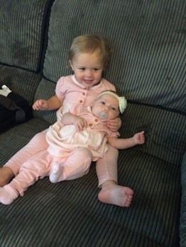 A toddler girl on a couch and her baby sister in her lap