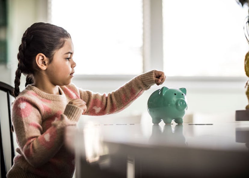 Young girl wearing a pink shirt while putting money in her green piggy bank on a wooden table