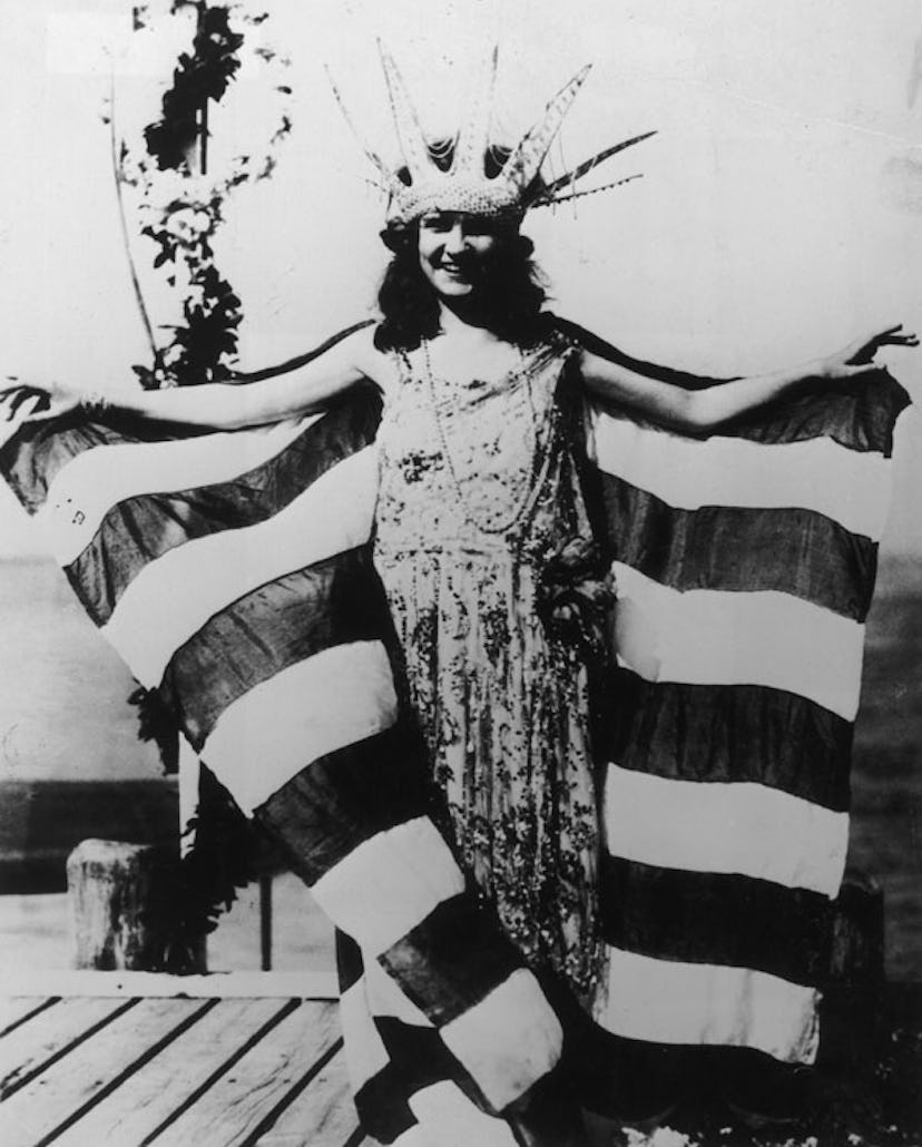 Margaret Gorman smiling, wearing a large Statue of Liberty crown and a striped cape, as the first Mi...