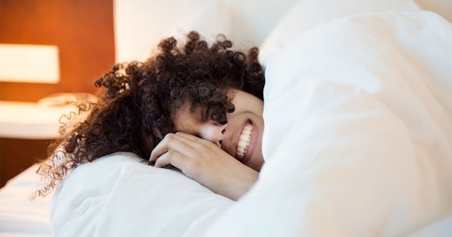 A girl lying in her bed, covered with white sheets, with a broad smile on her face alone to combat h...