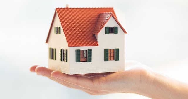 A model of a typical house held in a palm of a hand in front of a white background