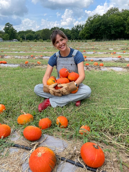 Jennifer Garner, sitting in a pumpkin field, holding a bunch of pumpkins in her hands and smiling