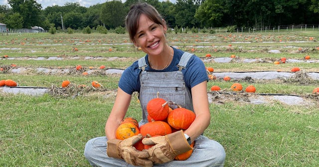 Jennifer Garner, sitting in a pumpkin field, holding a bunch of pumpkins in her hands and smiling