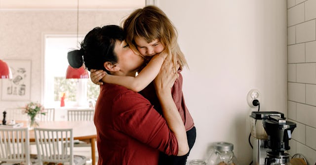 Mother in red shirt kissing her autistic daughter while holding her in arms inside their home