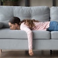Woman during her downtime laying on a gray couch looking unhappy