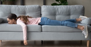 Woman during her downtime laying on a gray couch looking unhappy