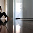 Stressed Woman wearing black shirt and pants sitting barefooted on the floor with her hand on her he...