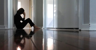 Stressed Woman wearing black shirt and pants sitting barefooted on the floor with her hand on her he...